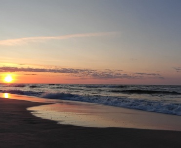 Pomarańczowe słońce chowające się nad Bałtykiem i fale dochodzące do brzegu tworzą romantyczny widok z plaży w Jastarni. To jeden z najpiękniejszych wieczornych krajobraz&oacute;w P&oacute;łwyspu Helskiego.